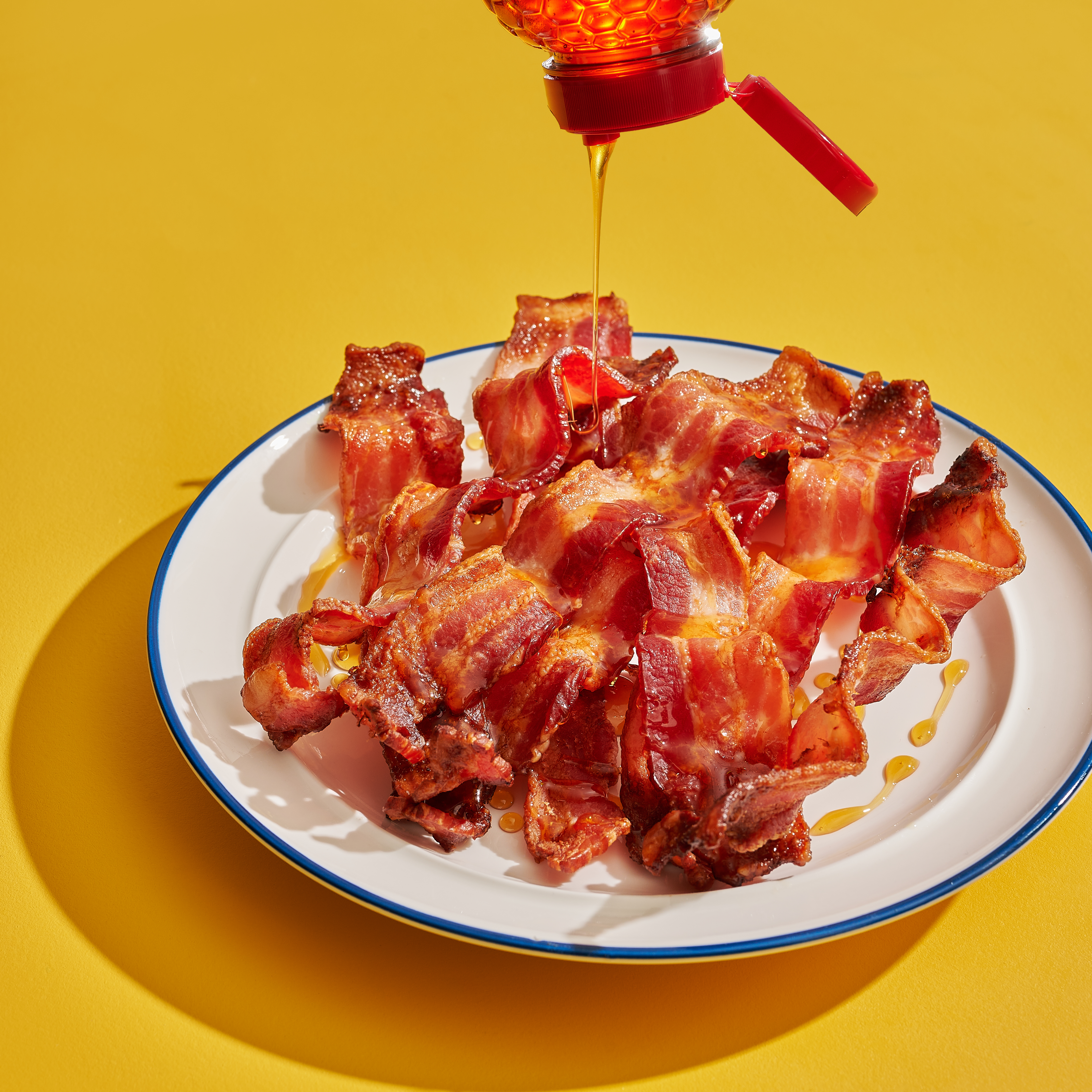 Plate of bacon with a bottle of Nate's hot honey drizzles over top of it.