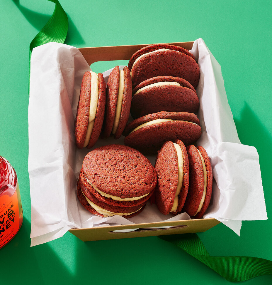 Red velvet whoopie pies in a box with a bottle of Nate’s honey on a green background.