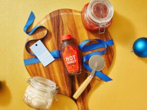 Nate’s hot honey bottle, a cheese board, ribbons, jars, and an ornament on a yellow surface.