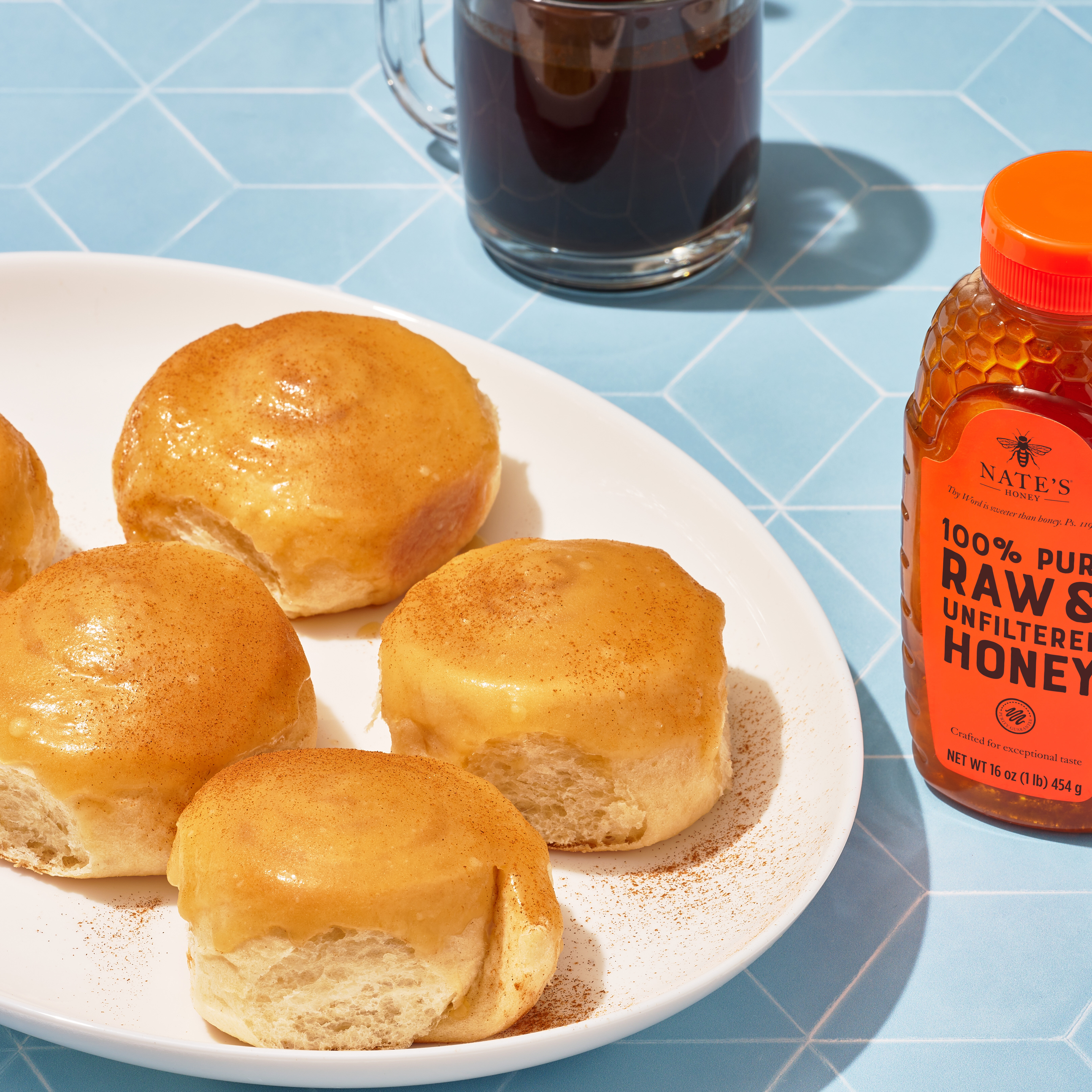 Golden honey buns on plates, with a bottle of Nate’s Honey, two forks and coffee.