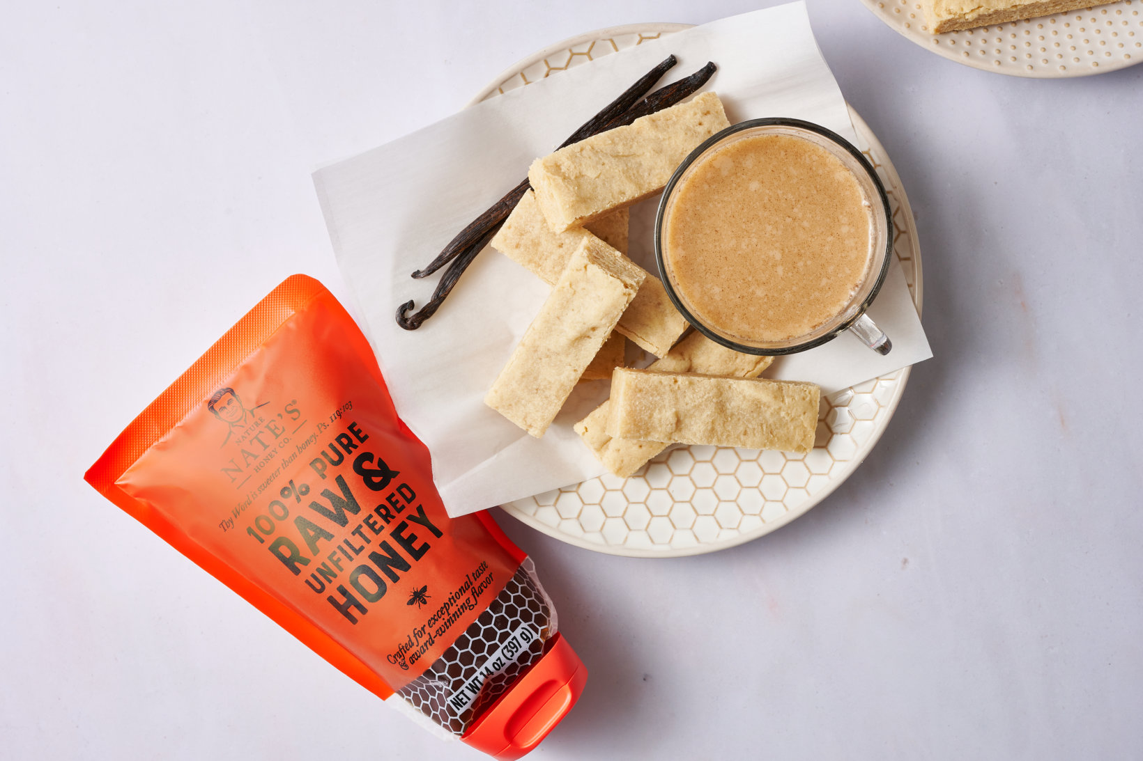 Vanilla shortbread cookies with coffee and a Nate's honey pouch on a patterned plate and white background.