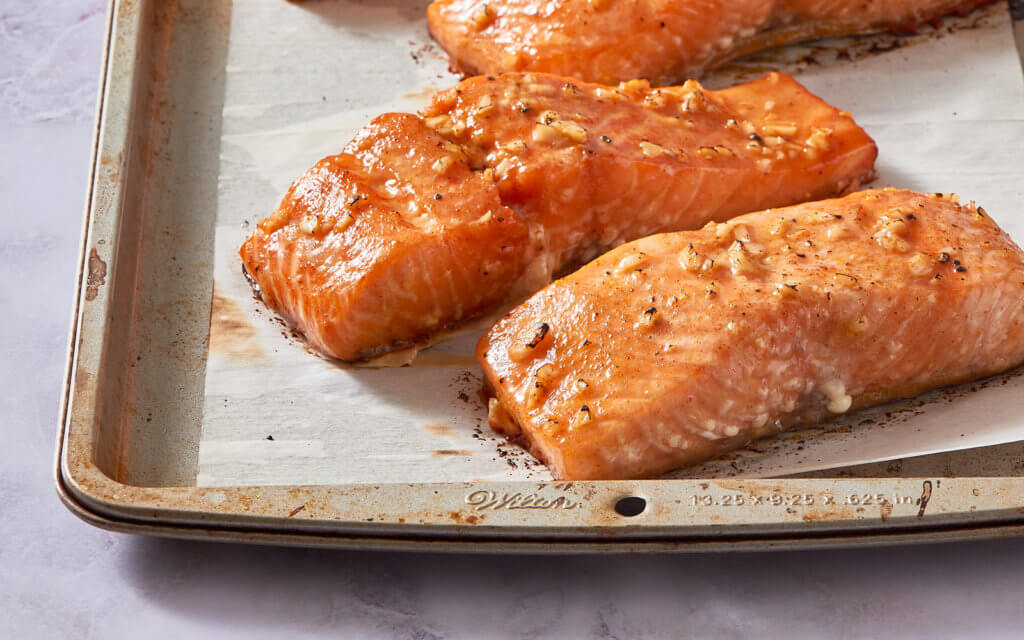 Seasoned, honey-glazed salmon fillets on a baking sheet,  ready for cooking.