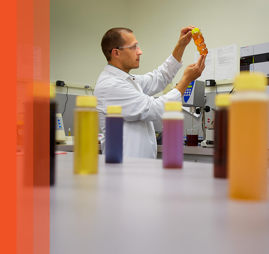 Scientist in lab coat examining a honey bottle in a lab with color samples.