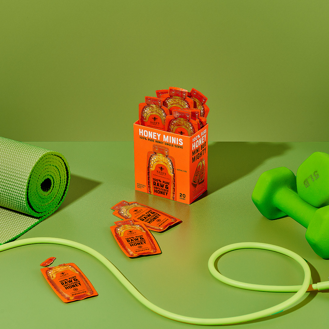 Box of Nate’s Organic Honey Minis surrounded by workout essentials like a yoga mat, dumbbells, and jump rope.