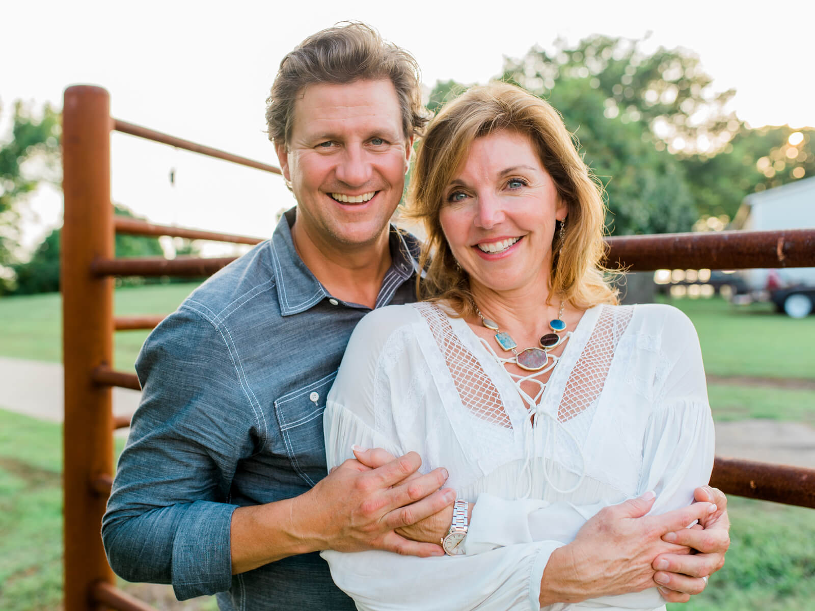 man and his wife embracing and smiling by a fence.