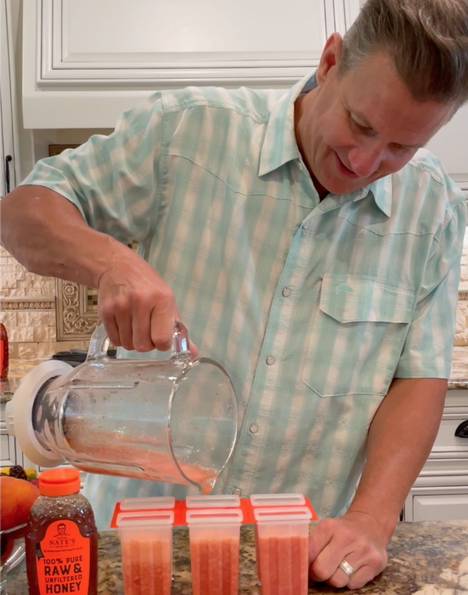The man Nature Nate pouring honey and fruit popsicles into molds on a counter with a bottle of Nate’s honey visible.