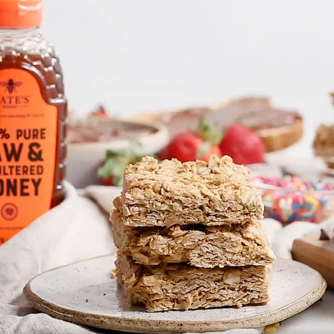 Stacked PB honey bars on a plate, bottle of Nate’s Honey and strawberries in background.
