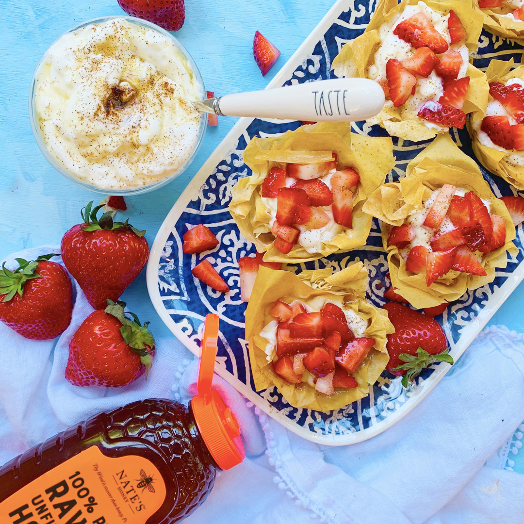Strawberry filo cups and cream, bowl of yogurt, and Nate's Honey bottle on a vibrant blue backdrop.