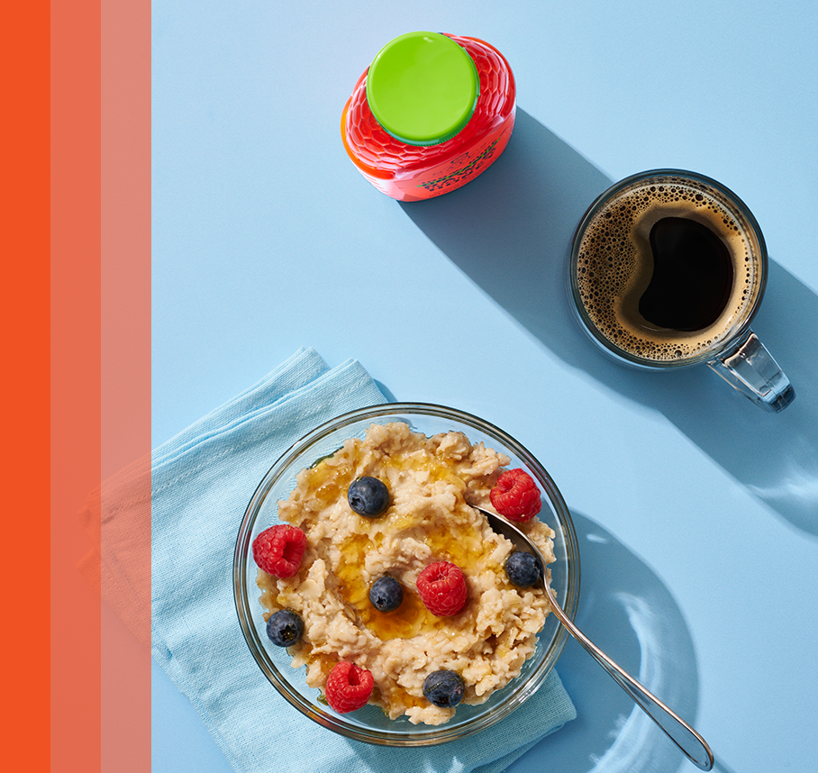 Bowl of oatmeal topped with berries and organic honey next to bottle of honey and mug of coffee.