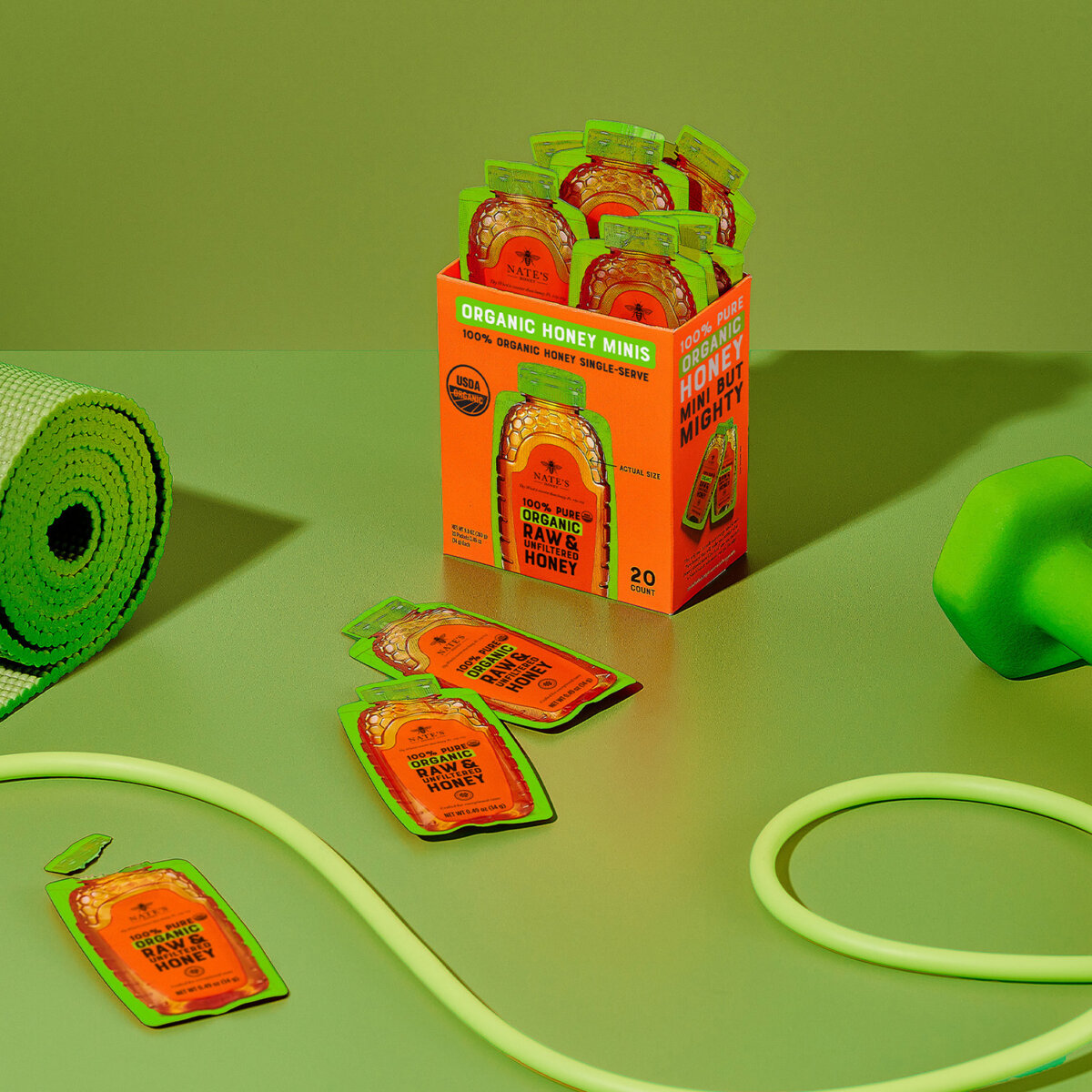 Box of Nate’s Organic Honey Minis surrounded by workout essentials like a yoga mat, dumbbells, and jump rope.