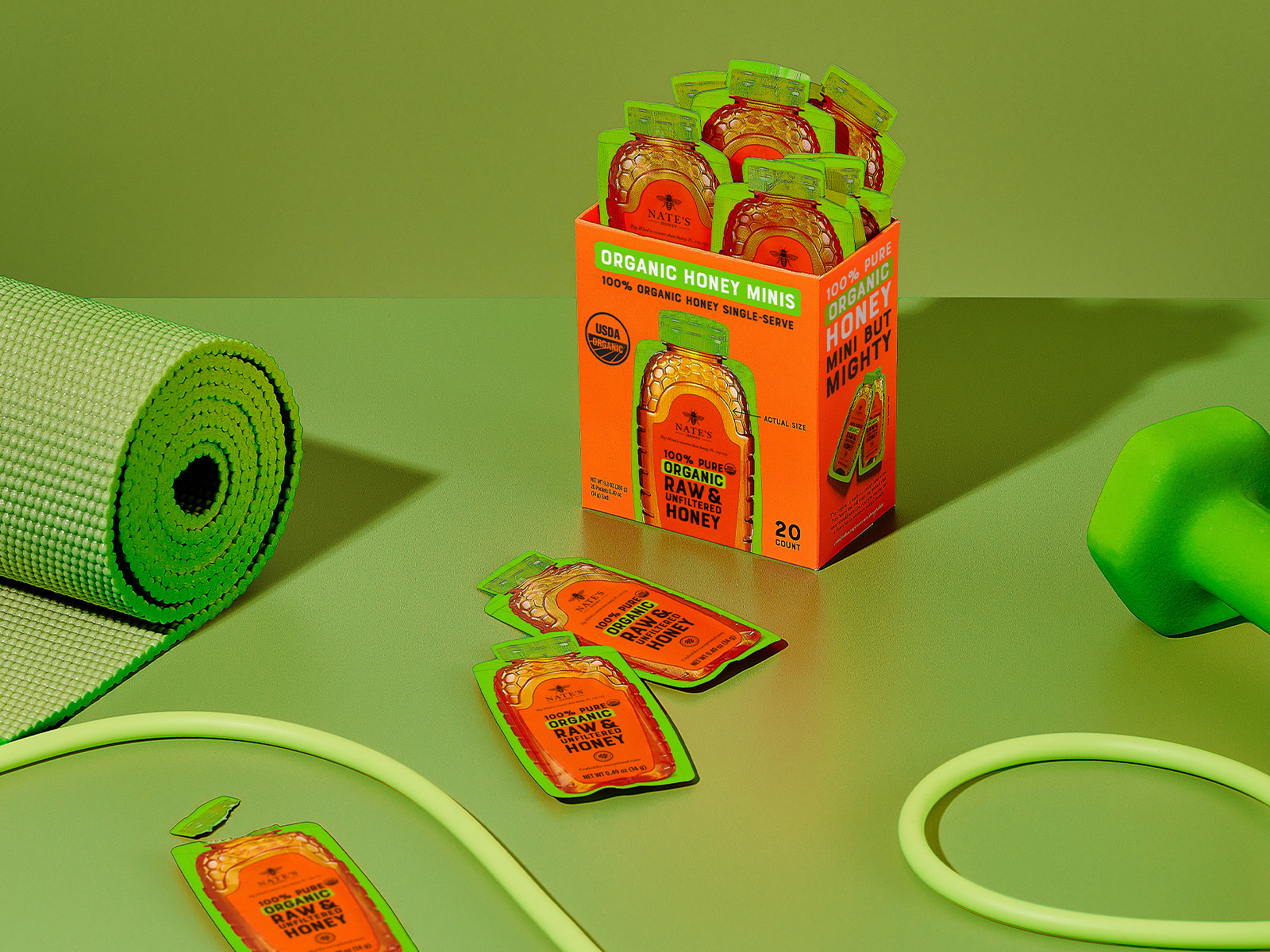 Box of Nate’s Organic Honey Minis surrounded by workout essentials like a yoga mat, dumbbells, and jump rope.