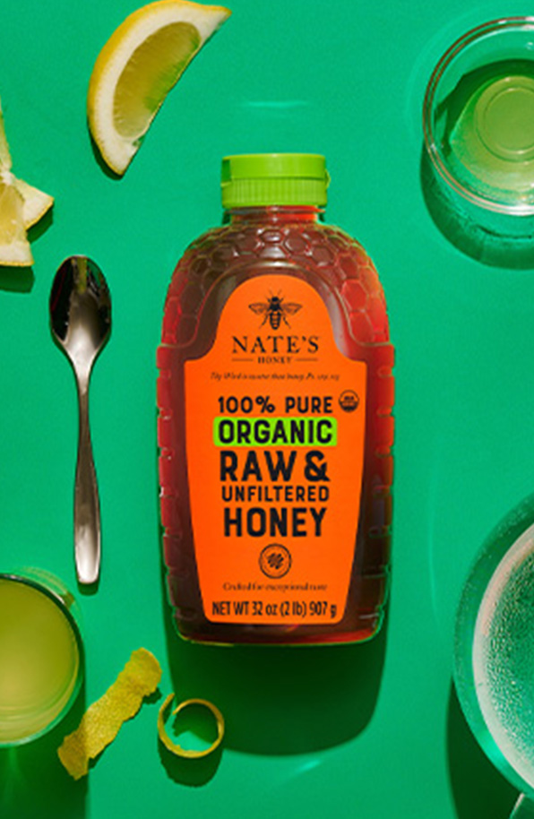 Organic honey bottle on green background surrounded by lemon slices.