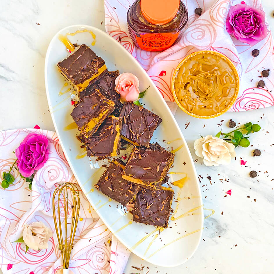 Platter with chocolate treats, Nate's honey bottle, peanut butter, and decorative roses on marble.