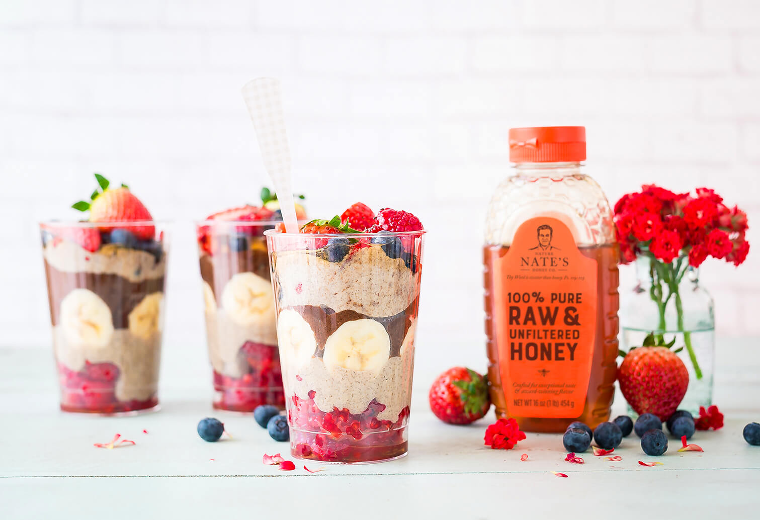 Four glasses of fruit parfaits with peanut butter, strawberries, blueberries and chocolate pudding on a marble counter.