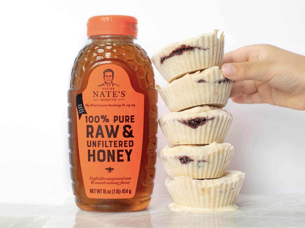 A hand stacking PB&J froyo bites next to a bottle of Nate's raw & unfiltered honey against a white background.