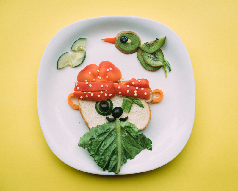Fun face-shaped toast with vegetables on a plate and yellow background.
