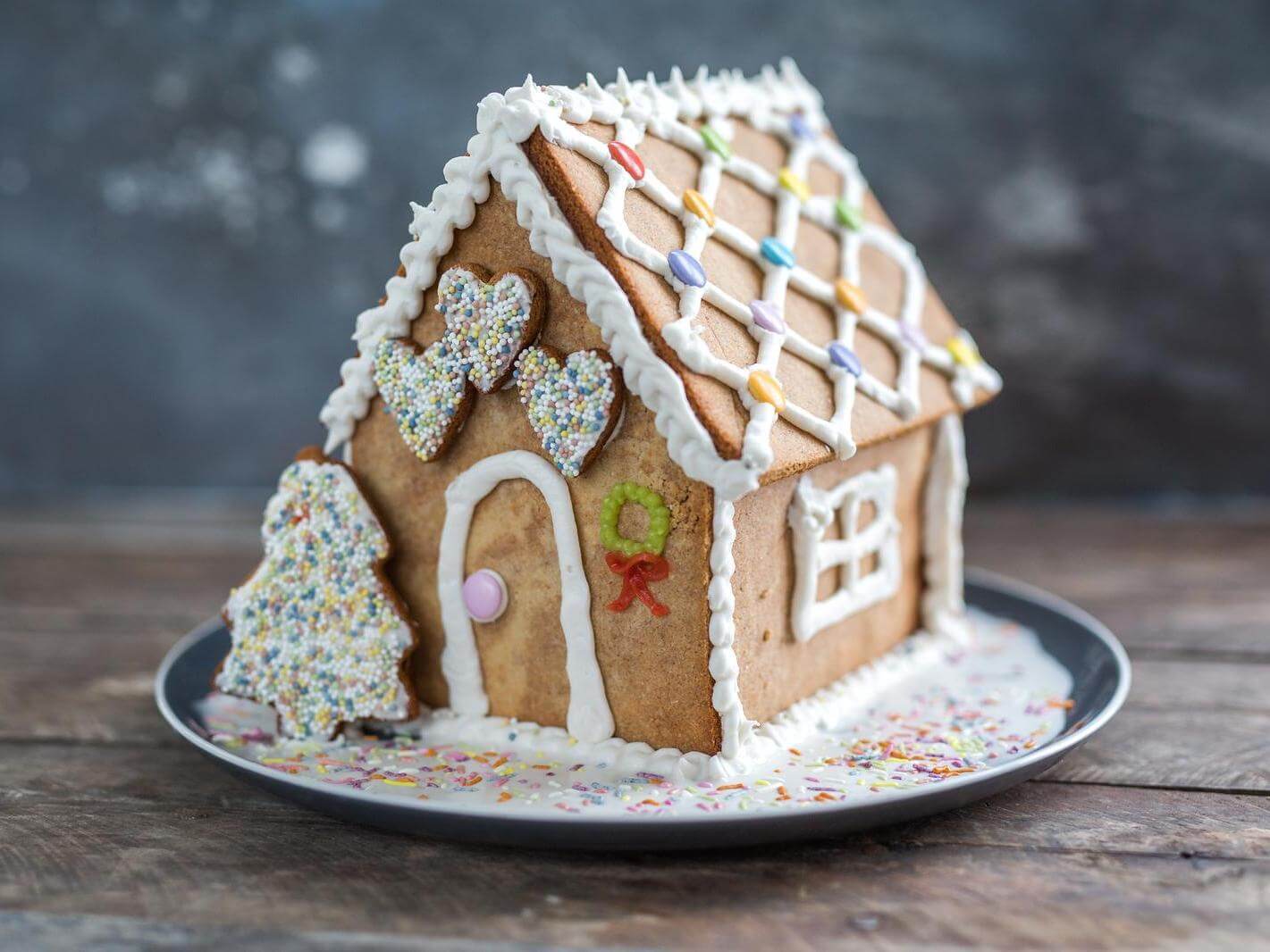 Delightful gingerbread house adorned with colorful candy and icing, displayed on a plate against a dark backdrop.