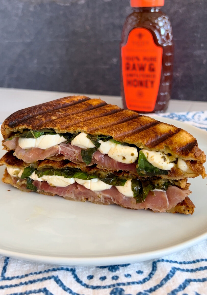 Grilled panini sandwich with basil, prosciutto and mozzarella cheese, next to a bottle of Nate’s Honey.