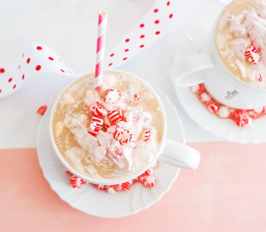 A festive peppermint drink with whipped cream and a striped straw in a white mug, surrounded by candy.
