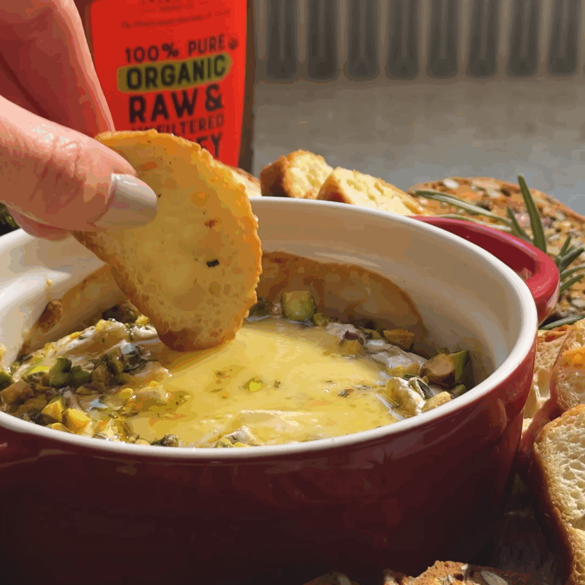 Dipping a cracker into melted baked brie with pistachios and honey.