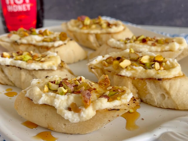 Crostini topped with ricotta cheese, chopped pistachio and hot honey drizzle.
