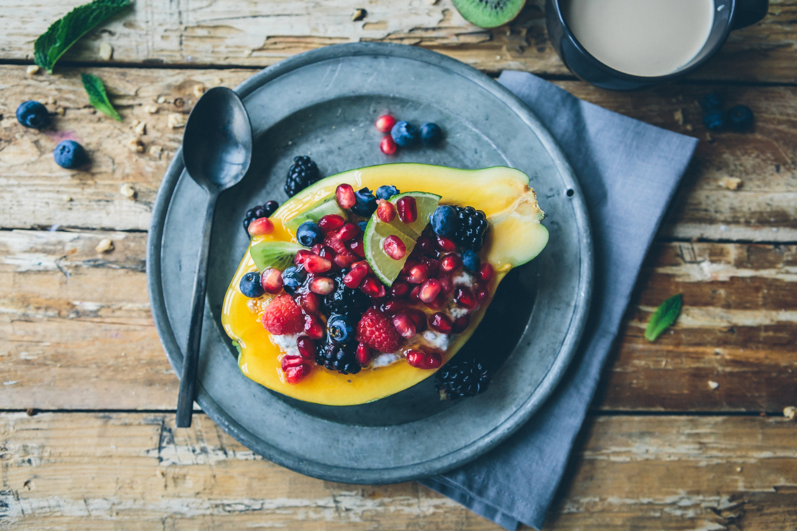 Chia pudding served in a papaya half topped with mixed berries on a pewter plate with a grey napkin, rustic table.