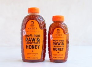 Two bottles of Nate's 100% Pure Raw & Unfiltered Honey on a white surface.