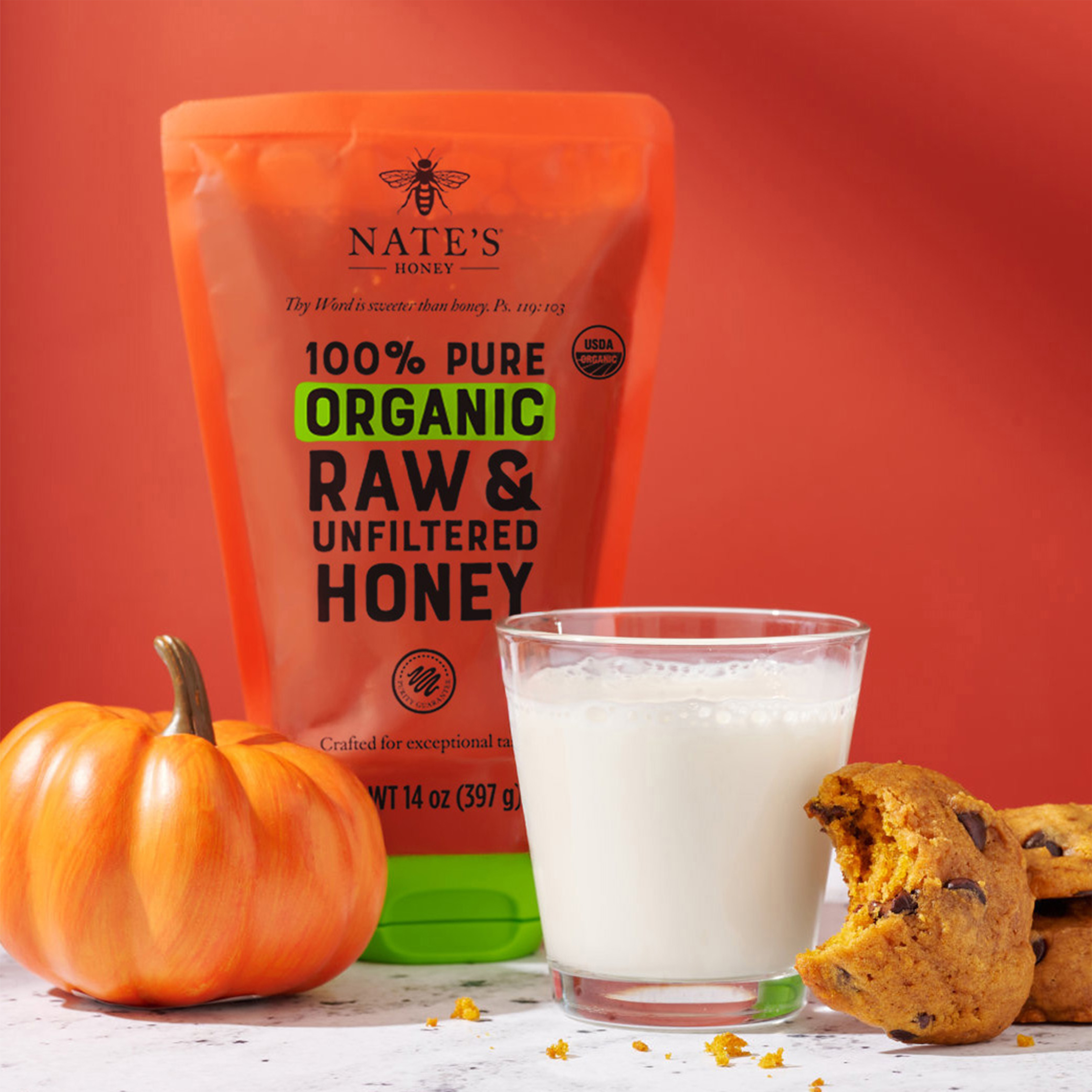 Glass of milk next to cookies, mini pumpkin and Nate's Organic Honey pouch.