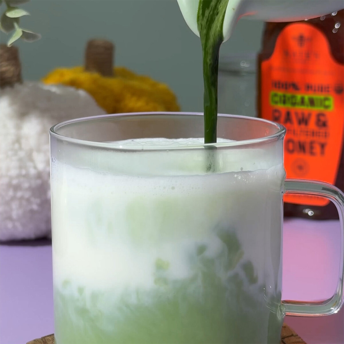 Clear mug of pumpkin matcha with organic honey bottle in background.