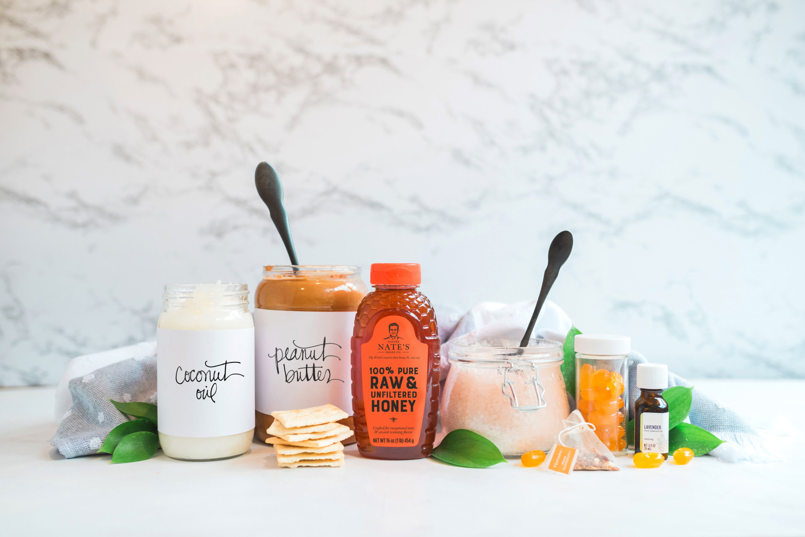 A selection of pantry staples including coconut oil, peanut butter and Nate's honey, displayed with fresh leaves.