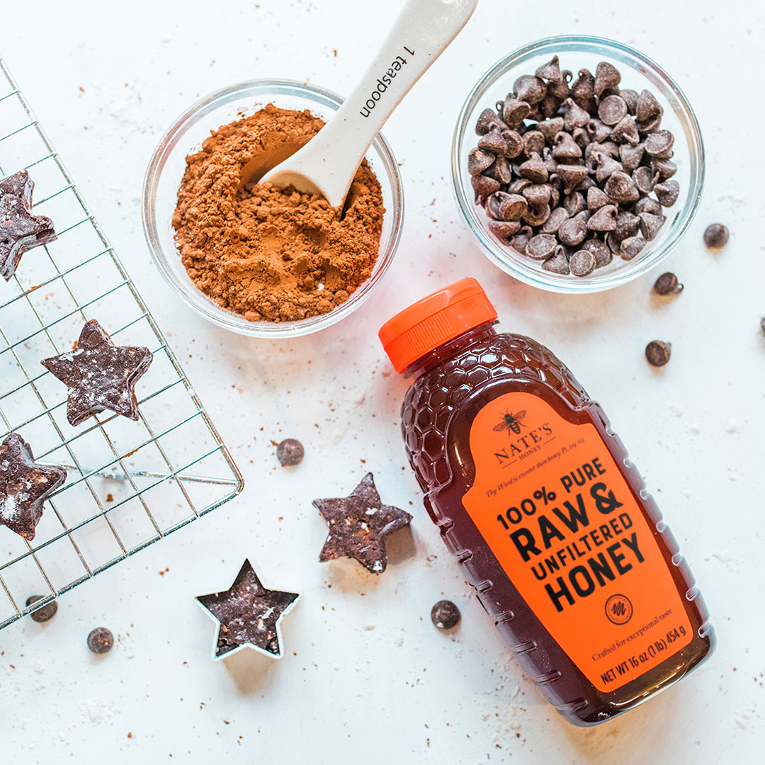 A bottle of Nate's Honey with baking ingredients and star-shaped fudge on a light countertop.