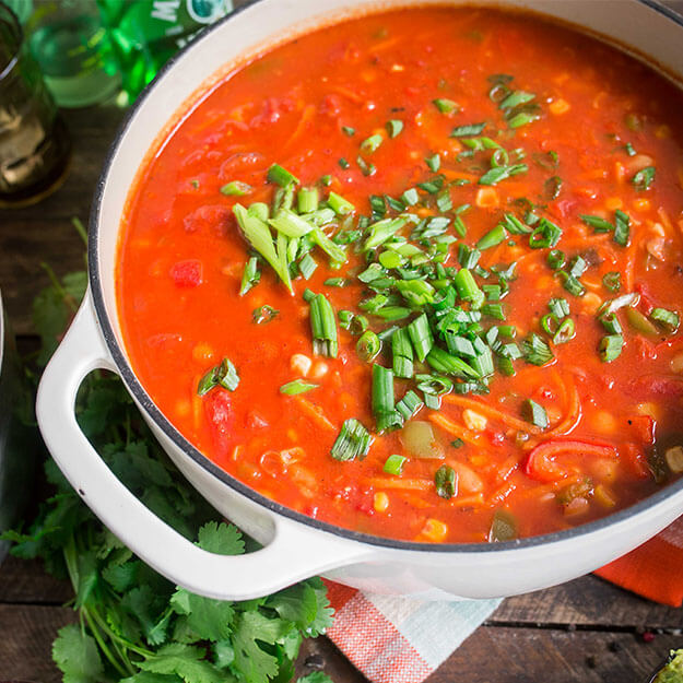 A white bean chili in a white pot on a wooden table, garnished with fresh herbs, evokes homestyle dining.