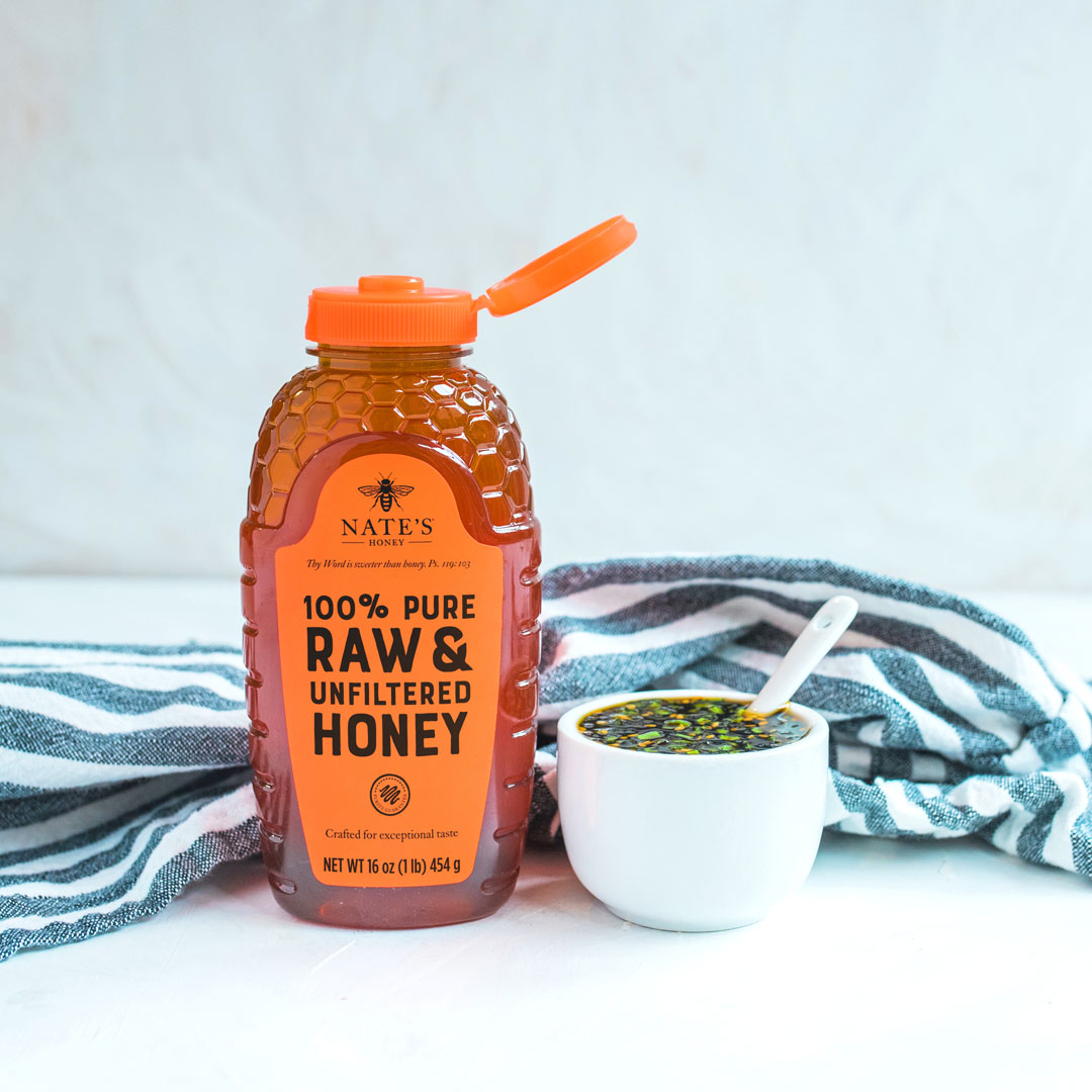 A bottle of Nate’s Honey with an orange cap and a bowl with honey soy dipping sauce on a striped napkin.