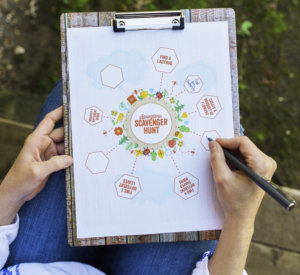 Hands holding a clipboard with a scavenger hunt game plan and floral design elements.