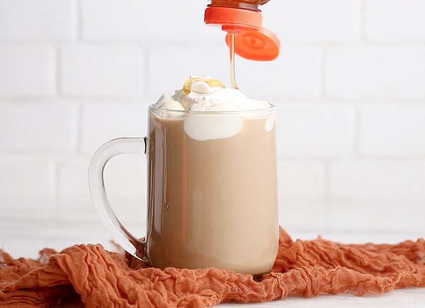 A mug filled with a Irish coffee topped with whipped  Cream, with Nate's honey being drizzled on top.