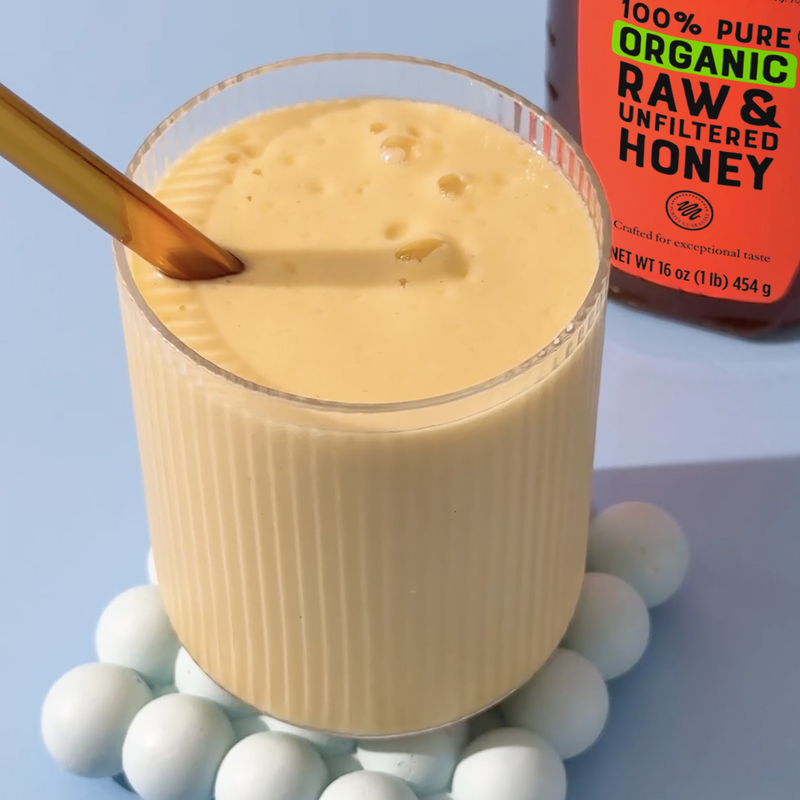 Glass of sunshine smoothie on coaster with bottle of Nate's Organic Honey in background.