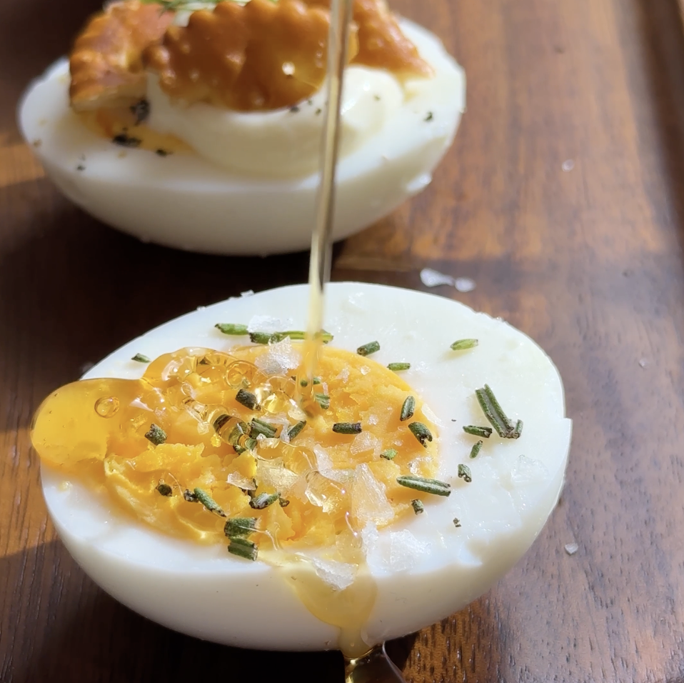 Hard boiled egg drizzled with rosemary, salt, and honey on wooden egg flight board.