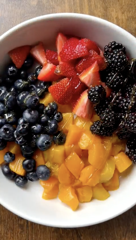 Top‑down view of a white bowl filled with blueberries, sliced strawberries, blackberries, and diced mango arranged in sections on a wooden surface.