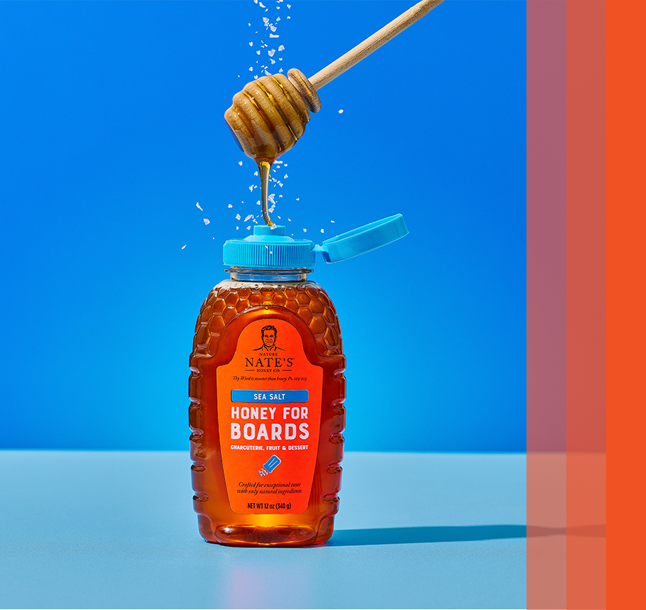 Sea Salt Flavored Honey bottle on blue background featuring honey dipper and sea salt sprinkle.