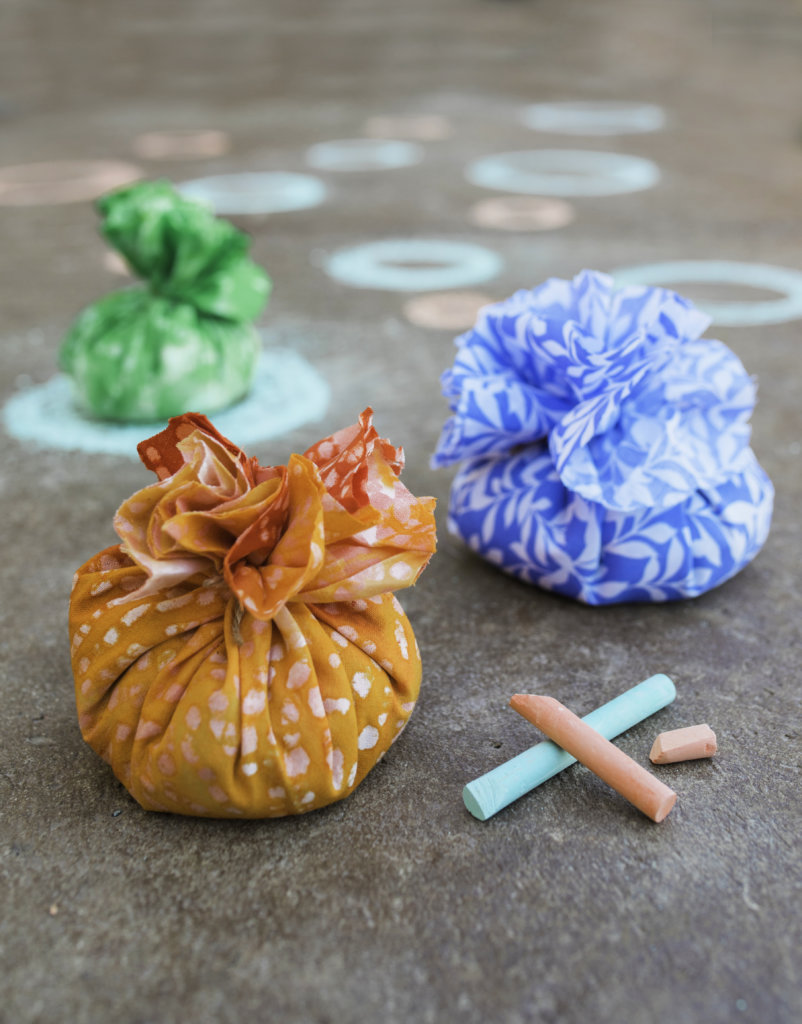 Colorful, round fabric bags filled with seeds with chalk and chalk-drawn circles on concrete.