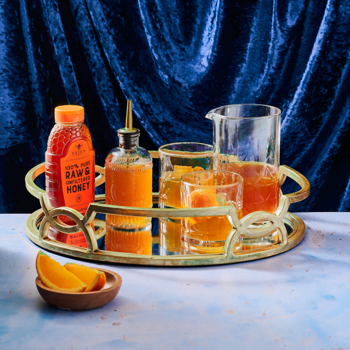 Brass tray with a bottle of Nate's Honey, a pitcher and two glasses filled with cocktails and a bottle of simple syrup.