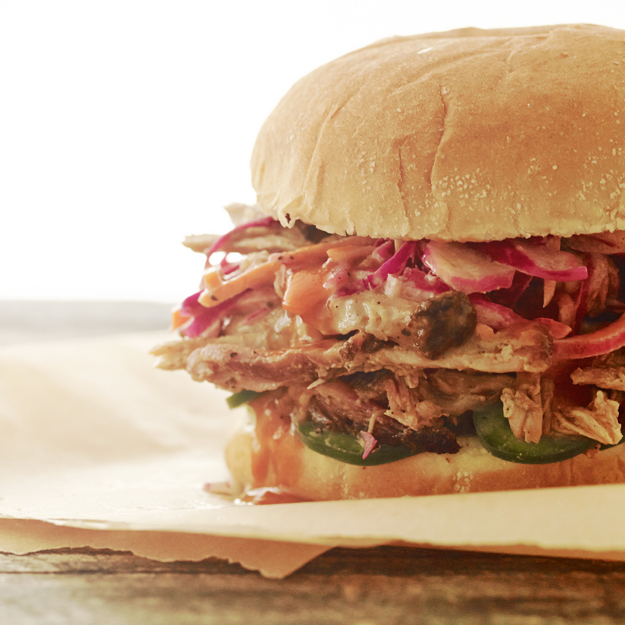 Pulled pork sandwich with slaw and pickles on parchment paper.
