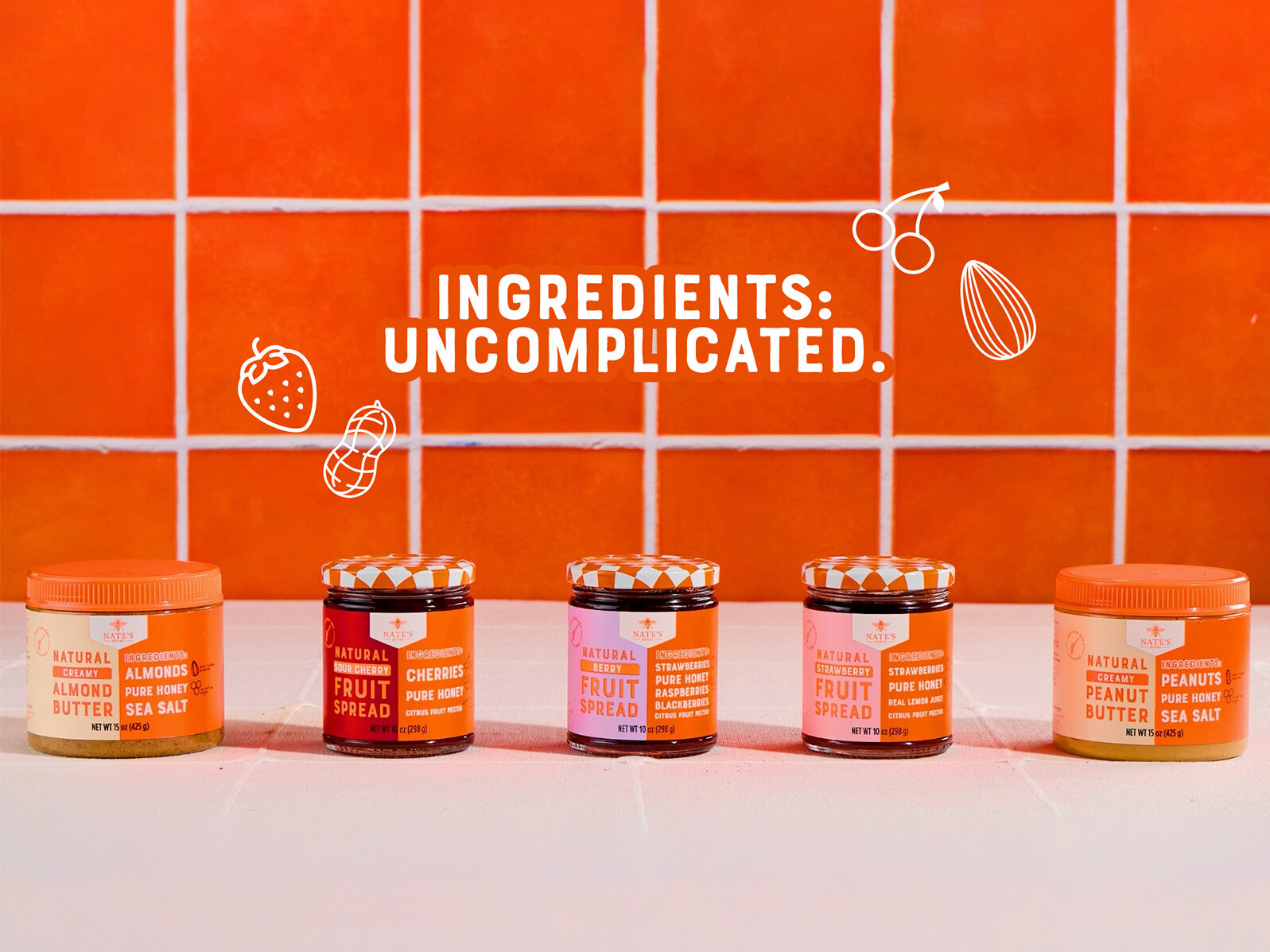 Jars of Nate’s Honey Fruit Spreads and Nut Butters arranged in front of an orange tile background with the text “Ingredients: Uncomplicated.” and simple line‑art illustrations of fruit and nuts.