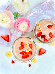 Smoothies with strawberries and patterned straws, surrounded by banana slices and flowers.