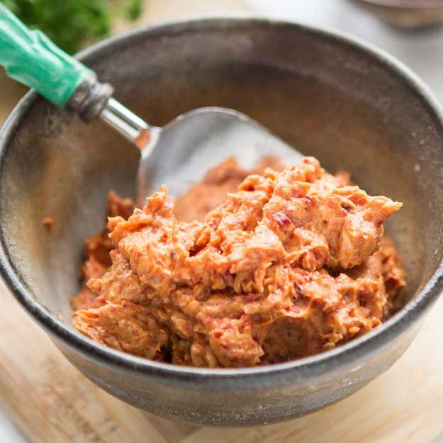 Bowl of sun-dried tomato and honey spread with a fork on a wooden surface.