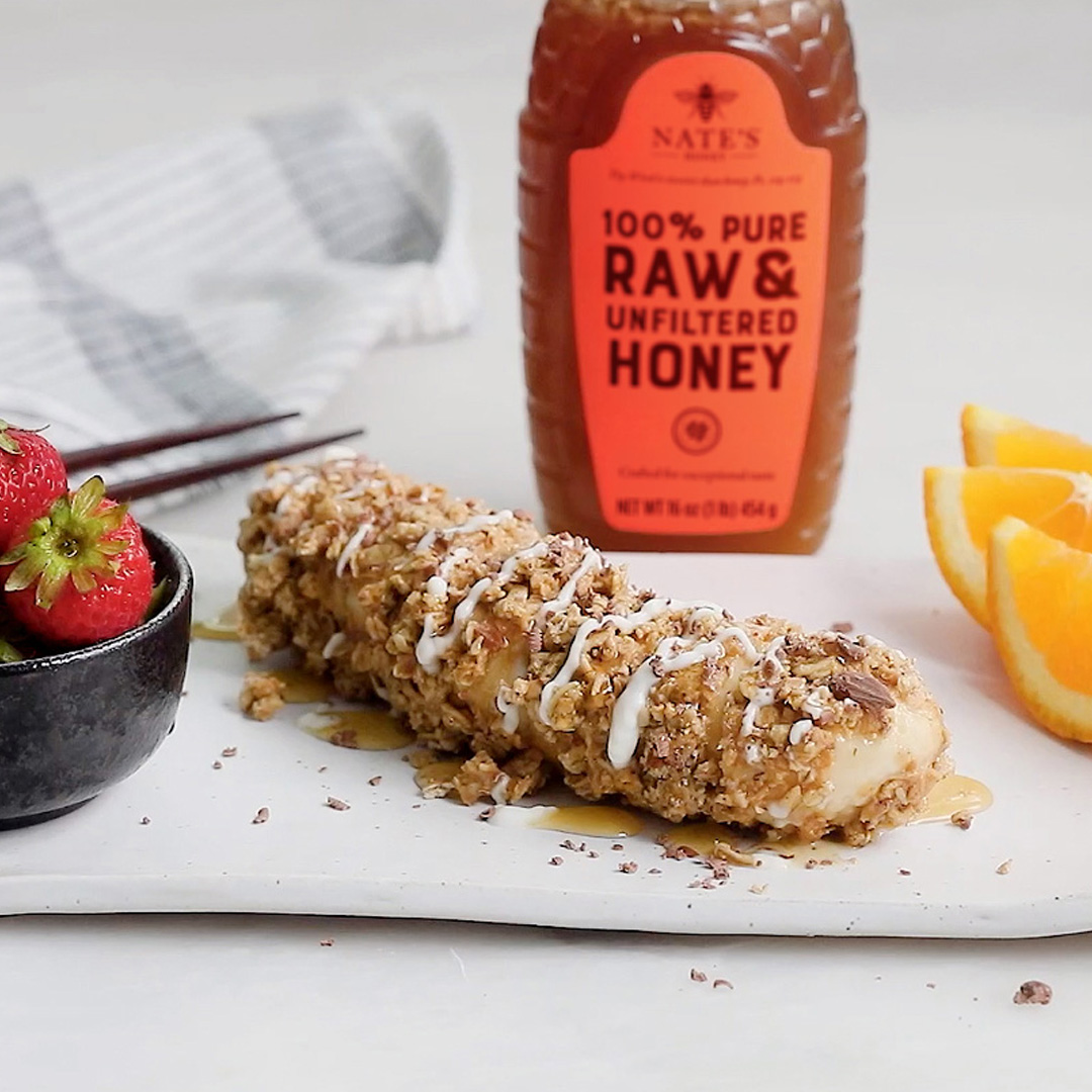 A granola bar drizzled with honey, fresh strawberries, orange slices, and a bottle of Nate's Honey.