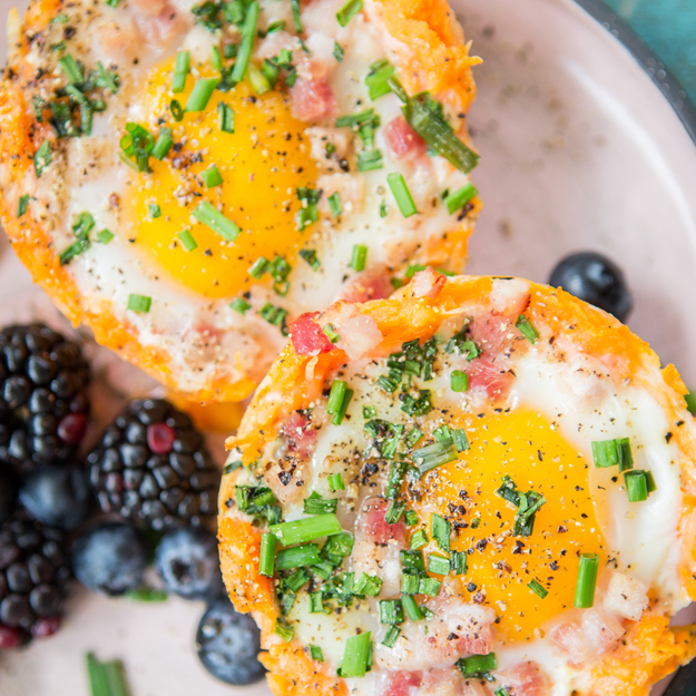Sweet potato cups filled with eggs, pancetta and cheese, garnished with chives, on a plate with berries.