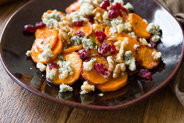Sweet potato rounds topped with blue cheese, cranberries and walnuts and drizzled with honey on a dark plate.