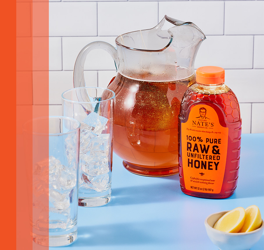 Clear pitcher filled with amber colored tea next to Nate's honey bottle, 2 glasses and small bowl of sliced lemons.