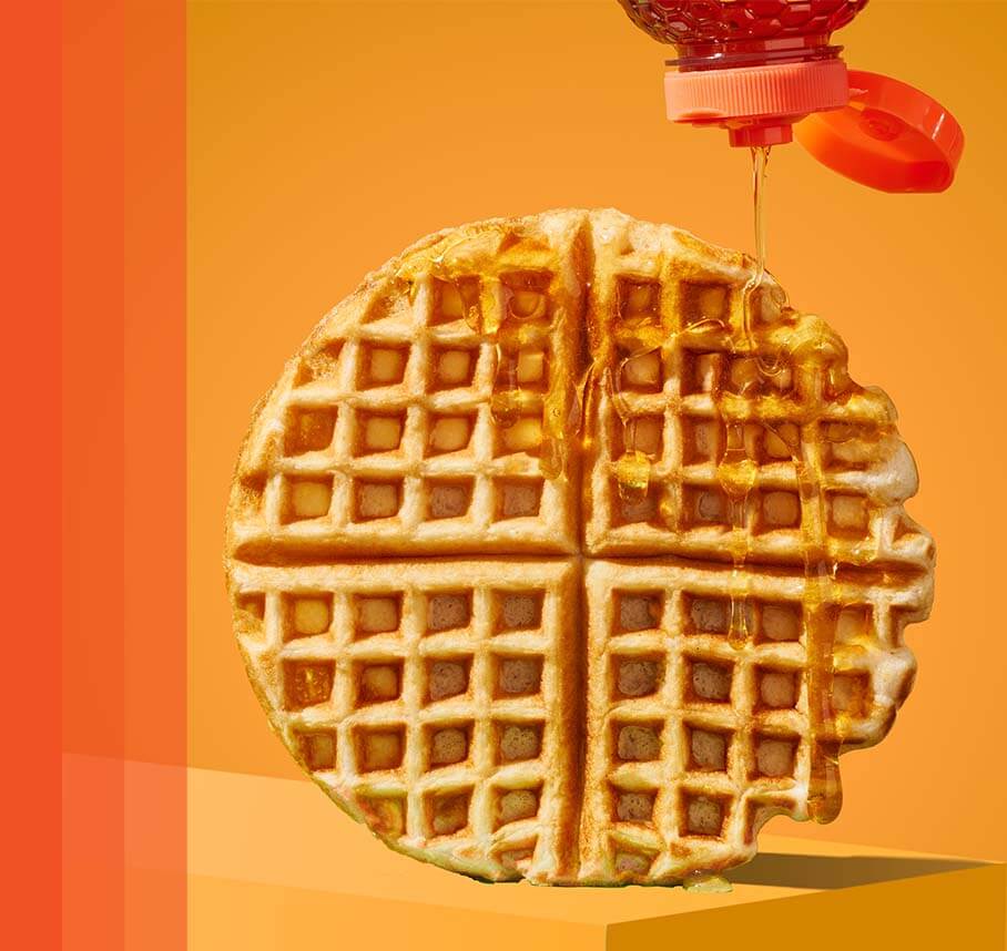 Golden honey drizzling onto a round waffle with a bite taken out.